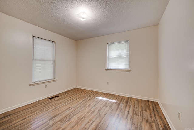 unfurnished room featuring visible vents, baseboards, a textured ceiling, and wood finished floors
