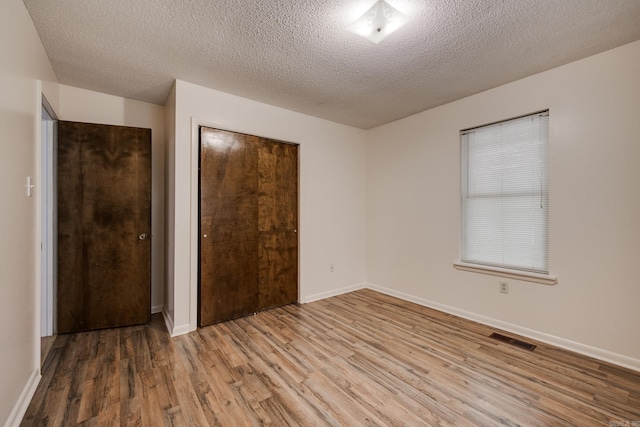 unfurnished bedroom with a textured ceiling, visible vents, wood finished floors, baseboards, and a closet