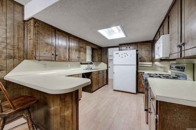 kitchen featuring a peninsula, white appliances, light wood-type flooring, a textured ceiling, and a sink
