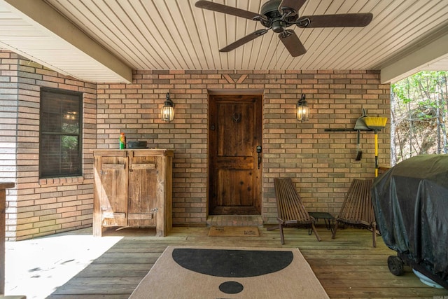 view of exterior entry with brick siding, a ceiling fan, and a deck