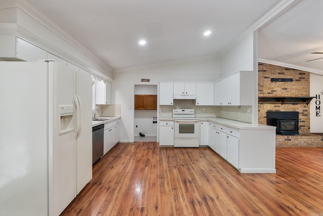kitchen with vaulted ceiling, white appliances, a wood stove, light wood finished floors, and backsplash