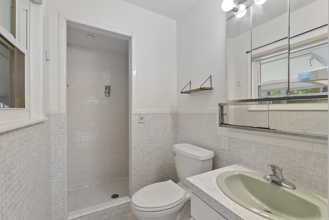 bathroom featuring toilet, tile walls, wainscoting, tiled shower, and vanity