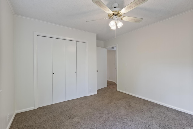 unfurnished bedroom featuring a closet, crown molding, baseboards, carpet flooring, and ceiling fan