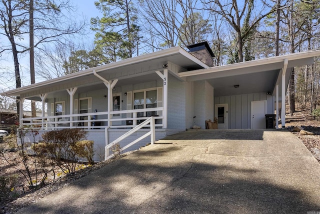 view of side of property featuring driveway, board and batten siding, covered porch, an attached carport, and brick siding