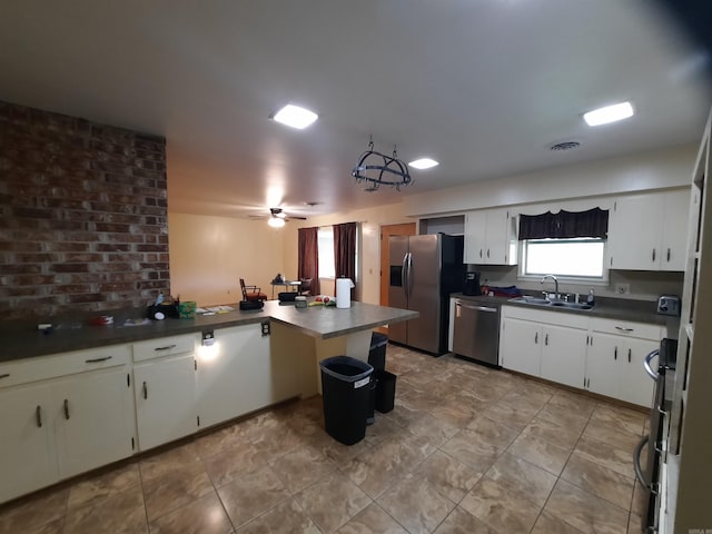 kitchen with a peninsula, a sink, dark countertops, a ceiling fan, and appliances with stainless steel finishes