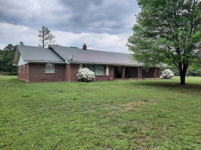 ranch-style house with a chimney, brick siding, roof with shingles, and a front yard