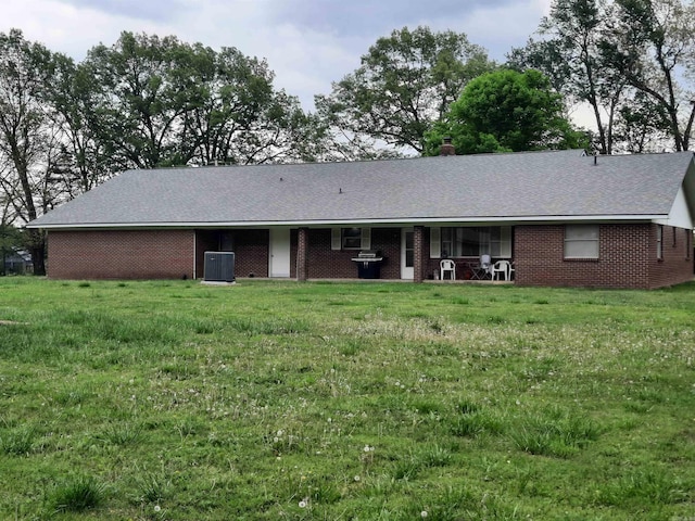 back of house with central AC, a chimney, brick siding, and a yard