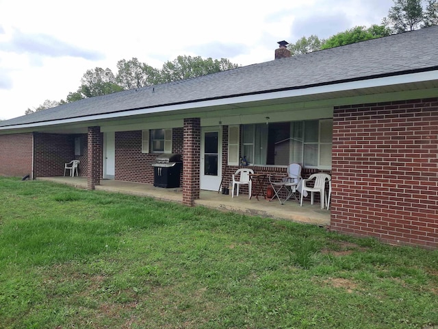 rear view of house with brick siding, a lawn, and a chimney