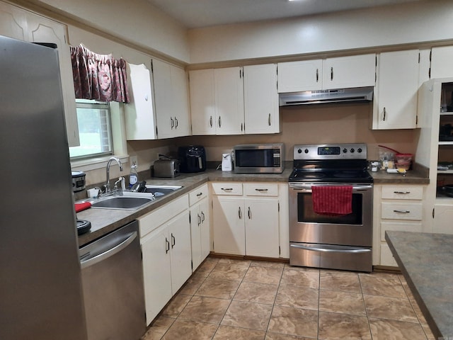 kitchen with under cabinet range hood, dark countertops, a sink, appliances with stainless steel finishes, and white cabinetry