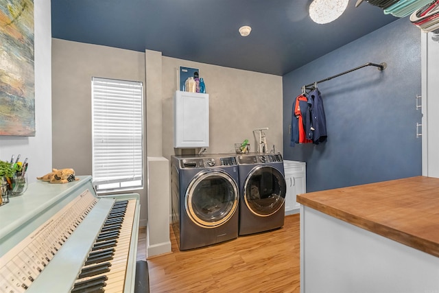 clothes washing area with light wood-style flooring, washer and clothes dryer, and cabinet space