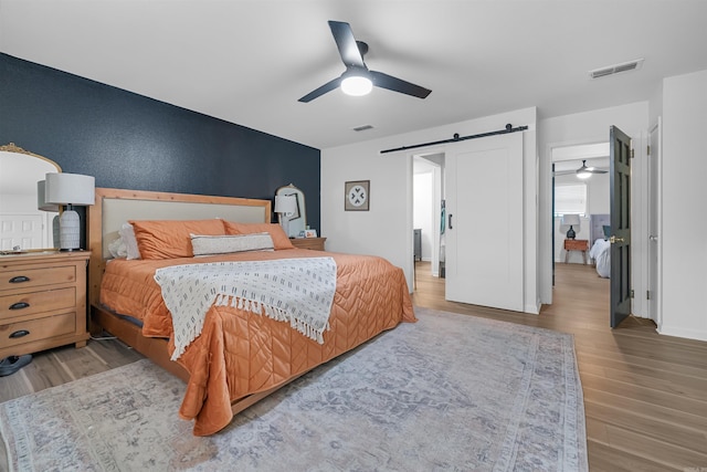 bedroom with wood finished floors, visible vents, ceiling fan, and a barn door