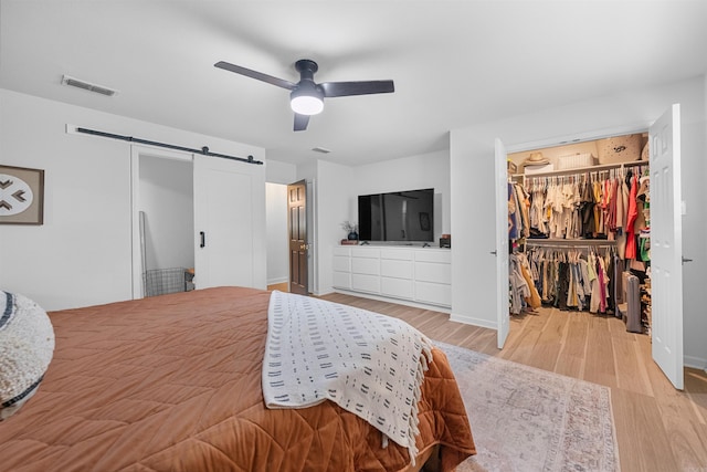 bedroom featuring light wood-style flooring, a barn door, visible vents, ceiling fan, and a walk in closet