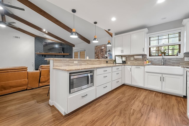 kitchen with a sink, vaulted ceiling with beams, light wood-type flooring, stainless steel microwave, and visible vents