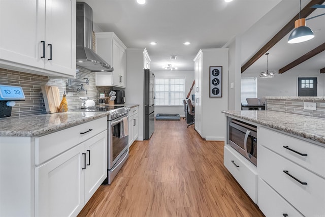 kitchen featuring wall chimney range hood, stainless steel appliances, white cabinets, and light wood-type flooring