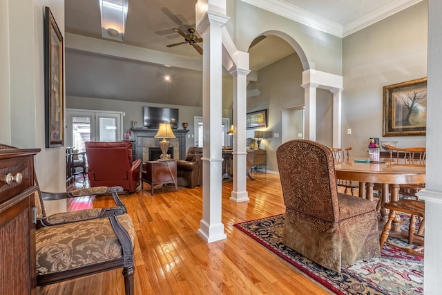 dining space with arched walkways, light wood-style floors, ornate columns, ceiling fan, and ornamental molding