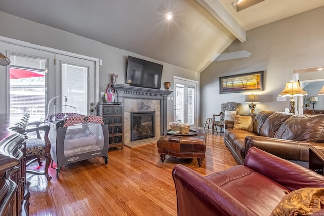 living area featuring lofted ceiling with beams, a healthy amount of sunlight, wood finished floors, and a tiled fireplace