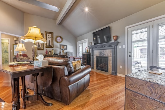living room with a tile fireplace, beamed ceiling, light wood-type flooring, baseboards, and high vaulted ceiling