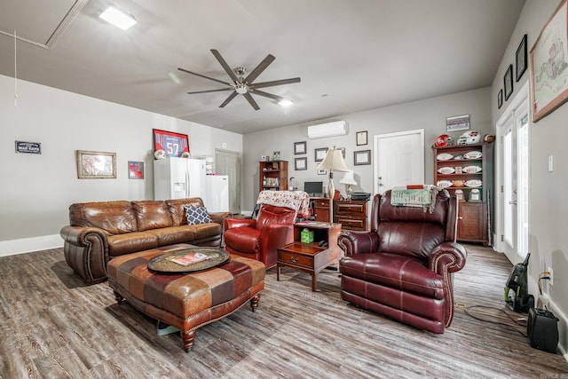 living area with wood finished floors, attic access, a wall mounted AC, ceiling fan, and baseboards