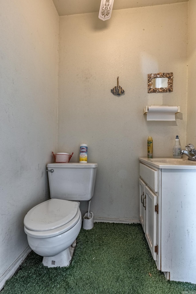 half bath featuring baseboards, vanity, and toilet