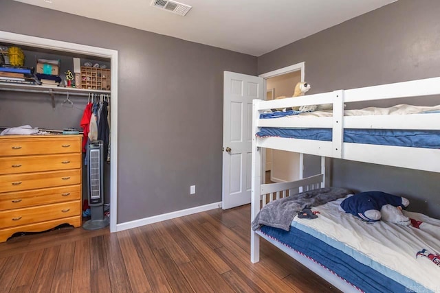 bedroom with a closet, wood finished floors, visible vents, and baseboards