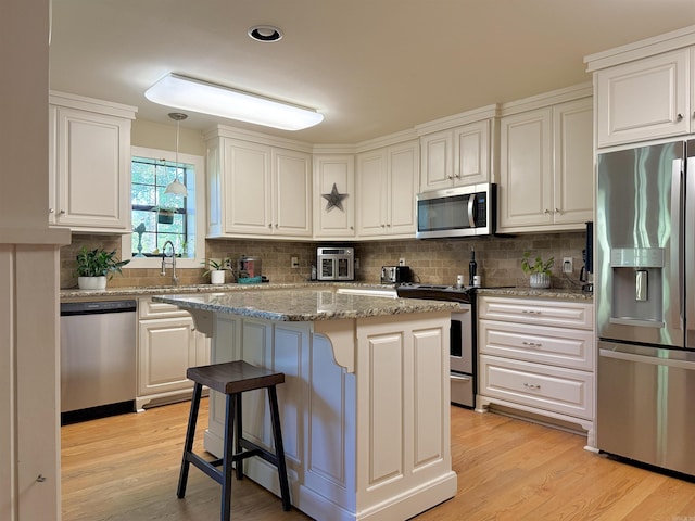 kitchen with light wood finished floors, tasteful backsplash, a kitchen island, and appliances with stainless steel finishes