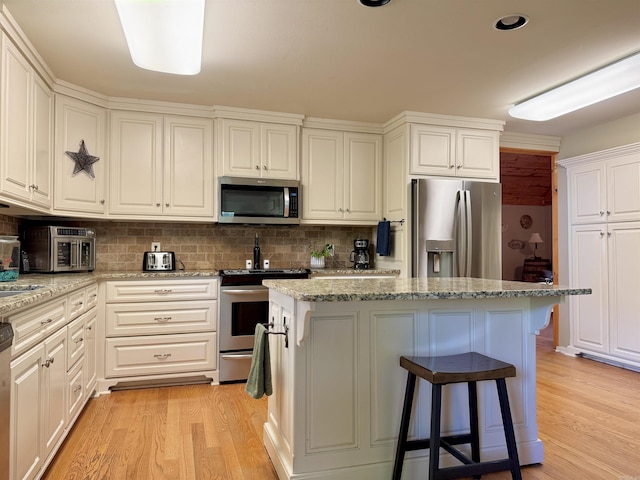 kitchen with white cabinets, stainless steel appliances, tasteful backsplash, light wood-type flooring, and light stone counters