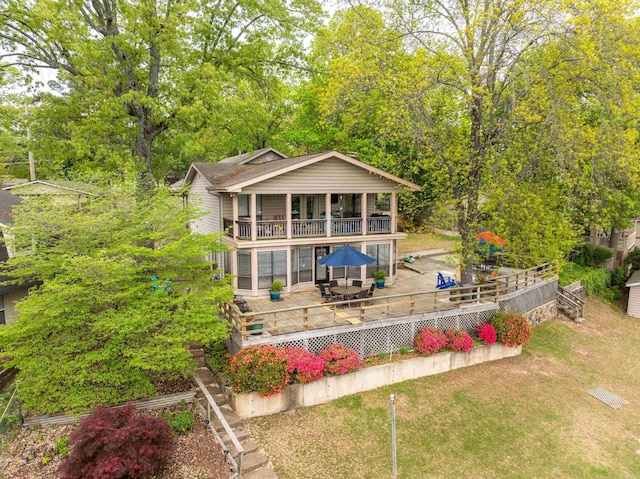 rear view of property featuring a lawn, a balcony, outdoor dining space, and a deck