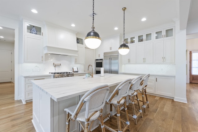 kitchen with white cabinets, light wood-style floors, a kitchen island with sink, tasteful backsplash, and appliances with stainless steel finishes