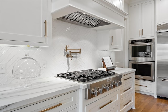 kitchen with white cabinets, backsplash, light stone counters, appliances with stainless steel finishes, and premium range hood