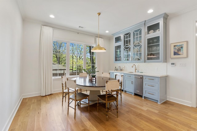 dining space with light wood finished floors, baseboards, wet bar, ornamental molding, and visible vents
