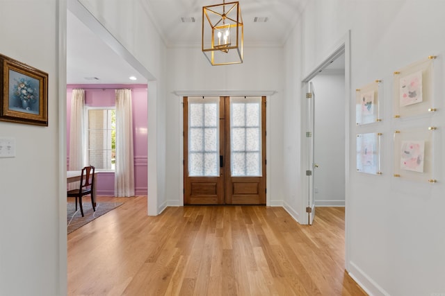 foyer featuring a notable chandelier, light wood-style floors, french doors, ornamental molding, and visible vents