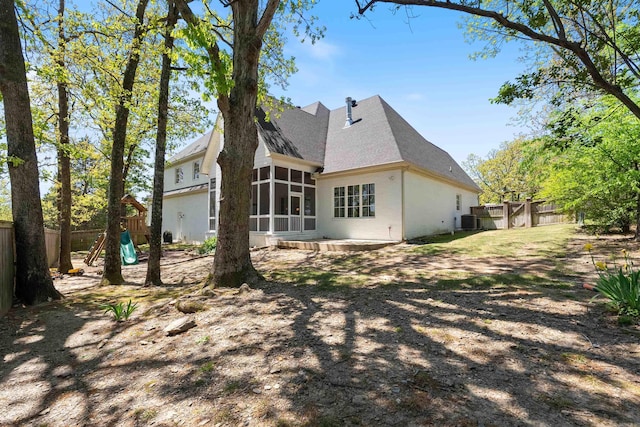 rear view of property featuring a fenced backyard, central AC unit, a sunroom, and a playground
