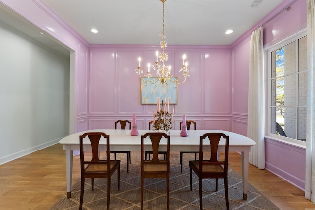 dining area featuring baseboards, light wood-style floors, a chandelier, and a decorative wall