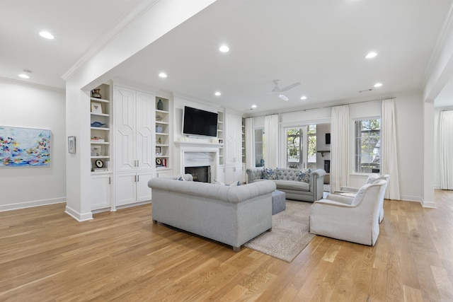 living area with crown molding, ceiling fan, light wood-style flooring, a fireplace, and baseboards