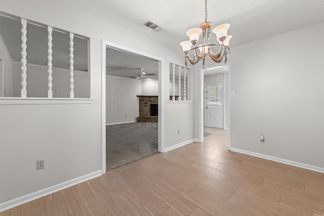 8302 Merriwood Ct, Sherwood, AR 72120 - spare room with a brick fireplace, wood finished floors, visible vents, a textured ceiling, and ceiling fan with notable chandelier