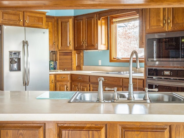 kitchen featuring light countertops, brown cabinetry, appliances with stainless steel finishes, and a sink