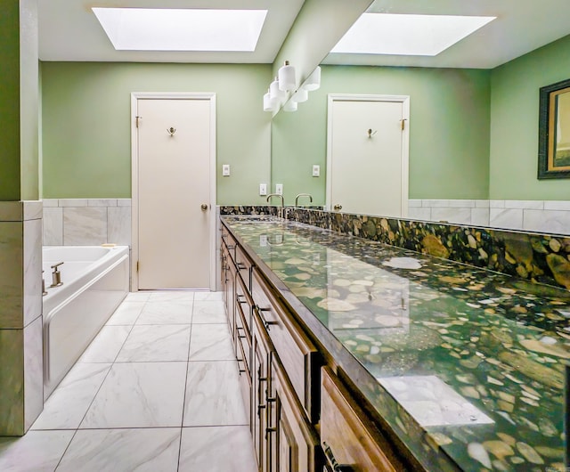 bathroom featuring a skylight, a bath, marble finish floor, and double vanity