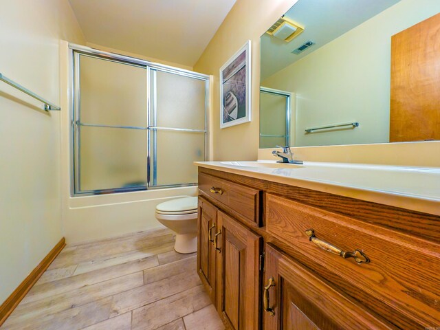 full bath featuring toilet, visible vents, wood finished floors, vanity, and enclosed tub / shower combo