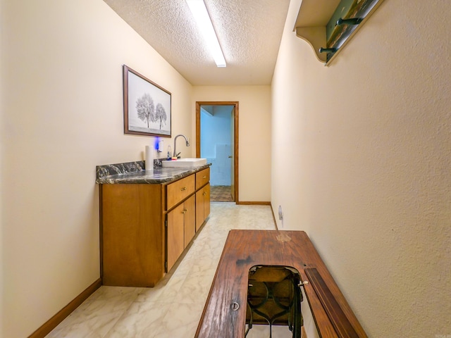 hallway featuring baseboards, a sink, and a textured ceiling