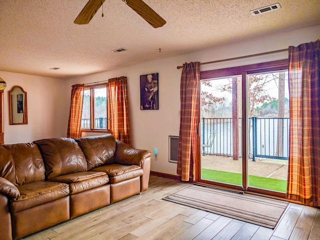 living room with light wood finished floors, visible vents, a textured ceiling, and ceiling fan