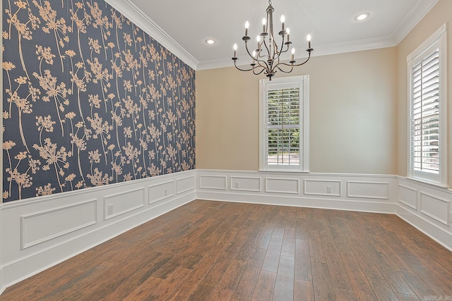 empty room featuring a healthy amount of sunlight, a wainscoted wall, dark wood-style floors, and a notable chandelier