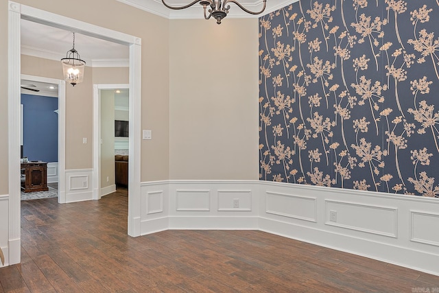 empty room featuring a decorative wall, a chandelier, a wainscoted wall, dark wood finished floors, and ornamental molding