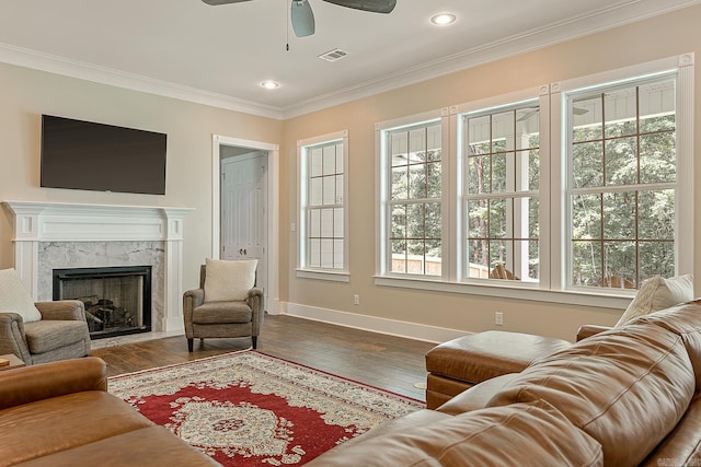 living room with crown molding, ceiling fan, a premium fireplace, baseboards, and visible vents