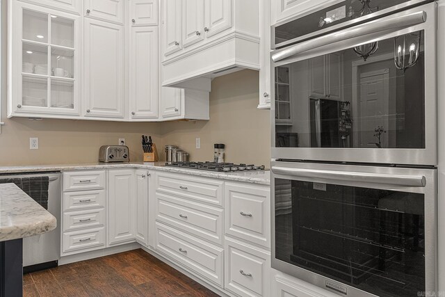 kitchen with white cabinets, light stone counters, stainless steel appliances, premium range hood, and dark wood-style flooring