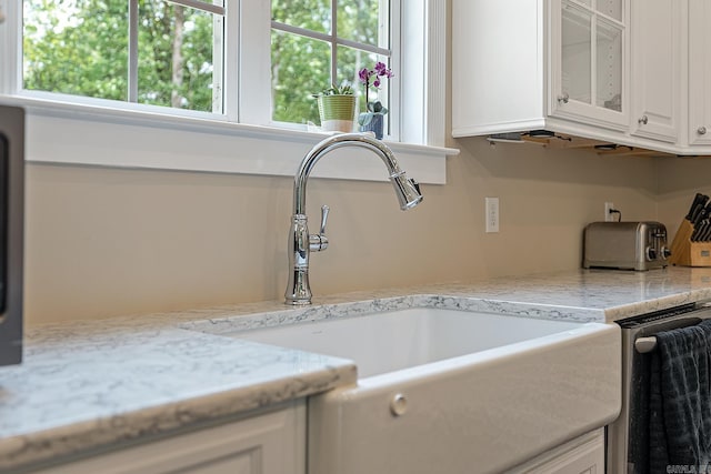 details with white cabinets, a sink, glass insert cabinets, light stone counters, and dishwasher