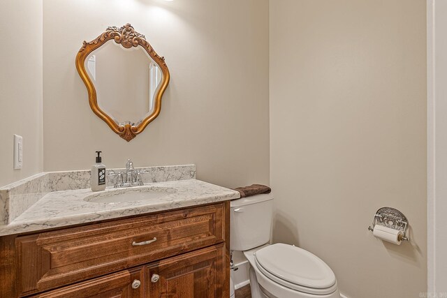 half bathroom with baseboards, toilet, and vanity