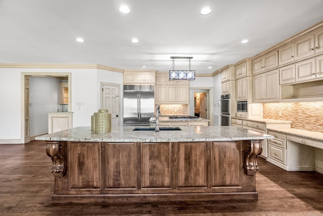 kitchen featuring built in appliances, cream cabinetry, a large island with sink, and a sink