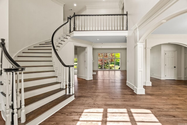 foyer entrance with a high ceiling, ornate columns, wood finished floors, arched walkways, and stairs