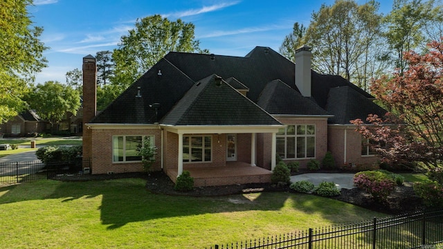 back of property featuring a chimney, brick siding, a patio area, fence private yard, and a yard