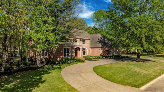 view of front facade with a balcony, driveway, a shingled roof, a front yard, and brick siding